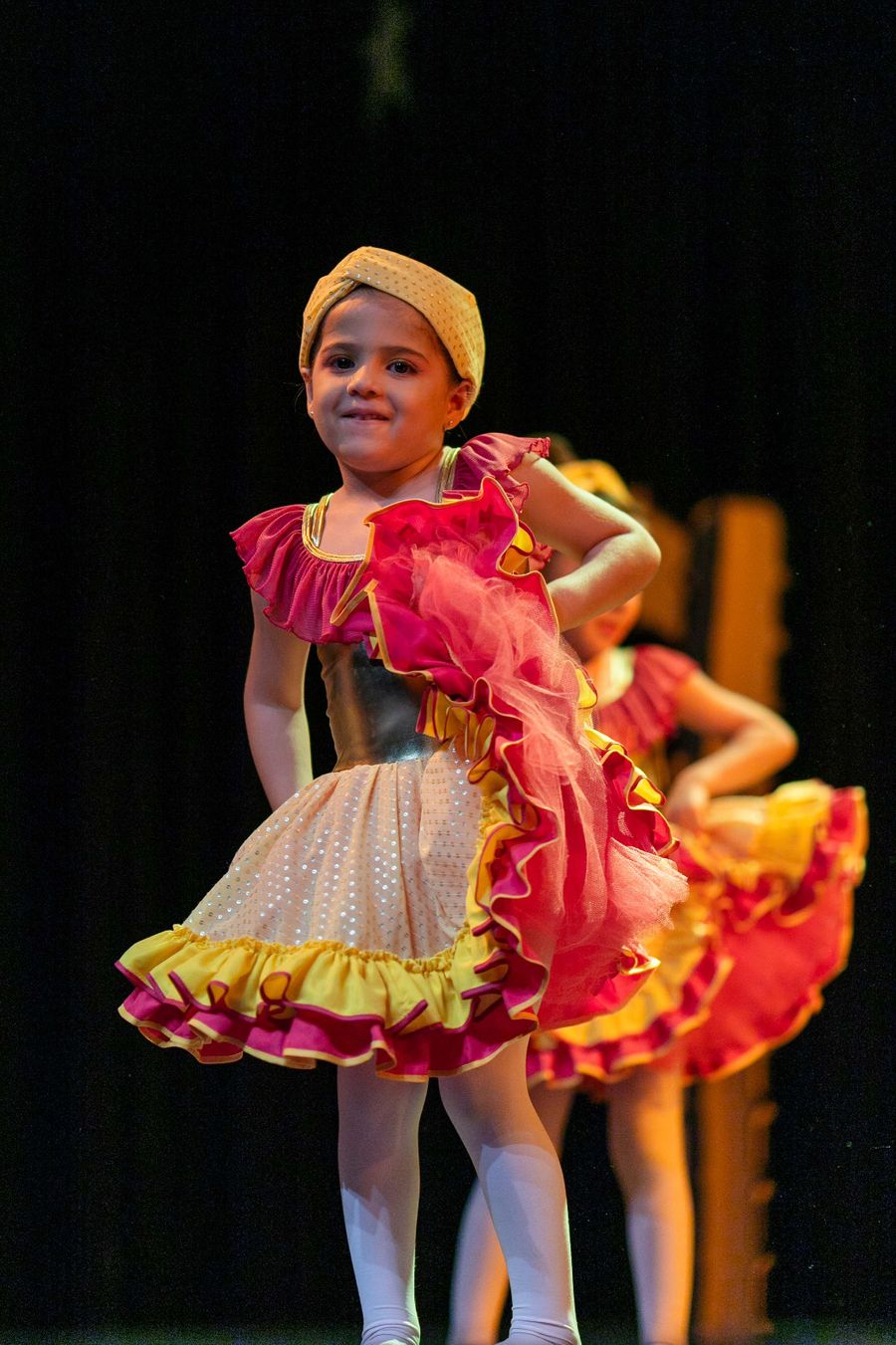 Aluna pequena sorrindo no palco, de vestido vermelho